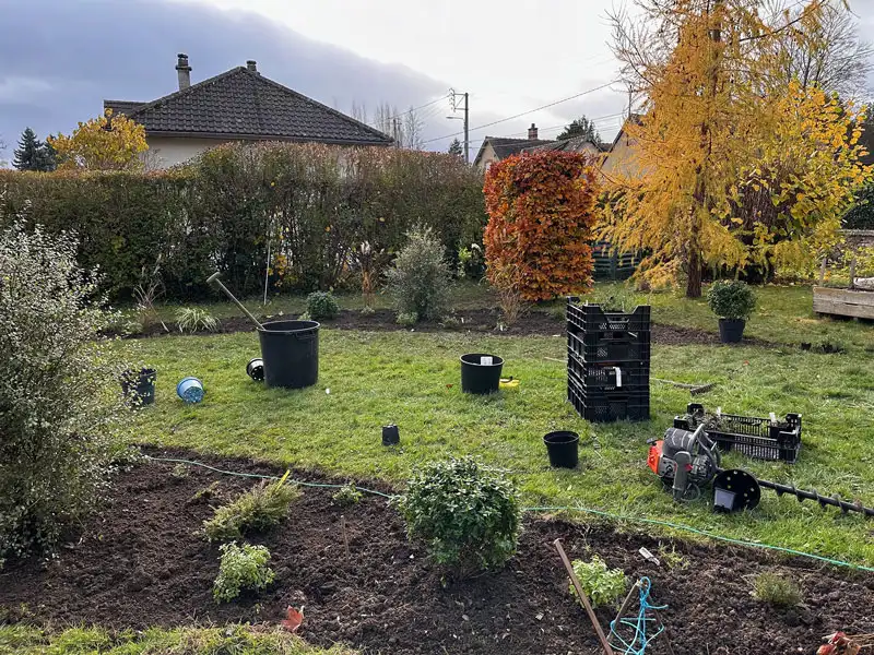 Garden being planted in autumn, with potted shrubs on the lawn