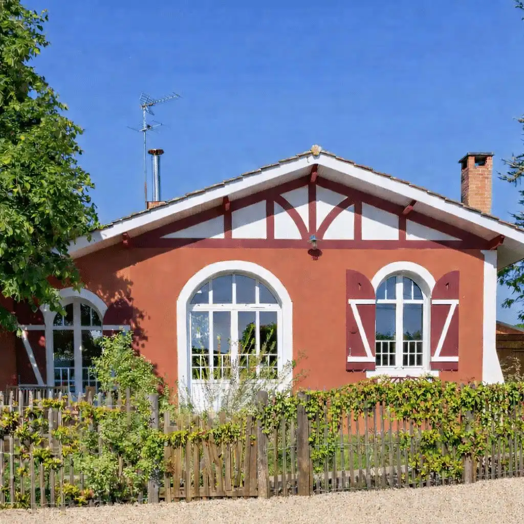Red brick house with arched windows, behind a planted wooden fence